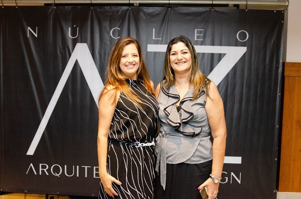 Duas mulheres posam para uma foto em frente a uma faixa que diz nucleo