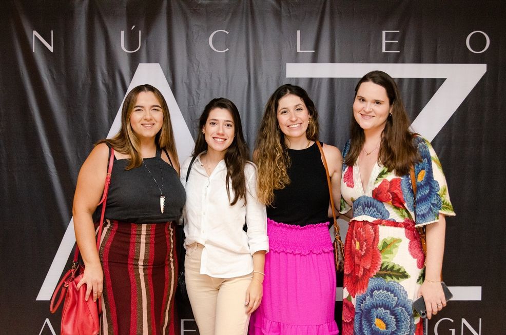 Quatro mulheres estão posando para uma foto em frente a uma placa que diz nucleo.