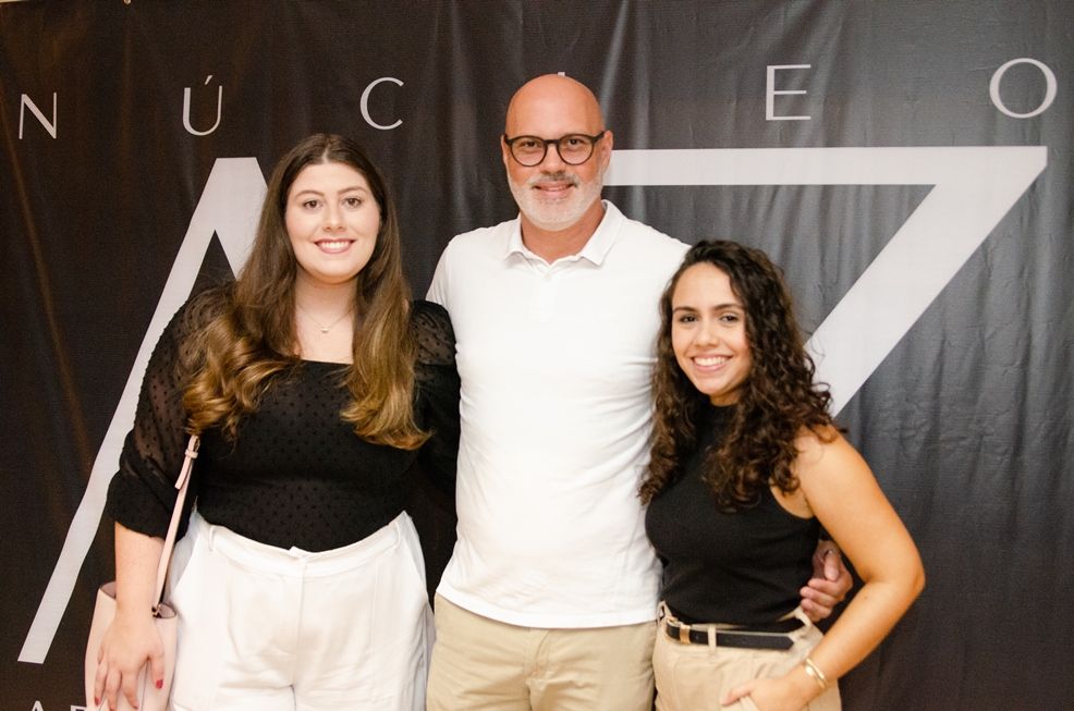 Um homem e duas mulheres estão posando para uma foto em frente a uma placa que diz nuc