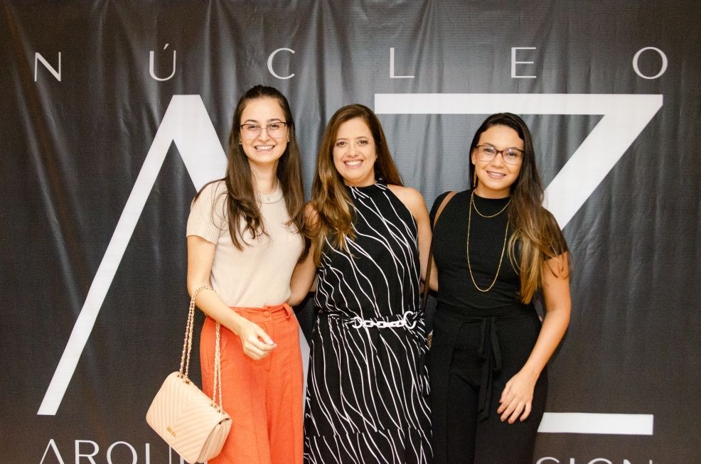 Três mulheres posando para uma foto em frente a uma placa que diz nucleo