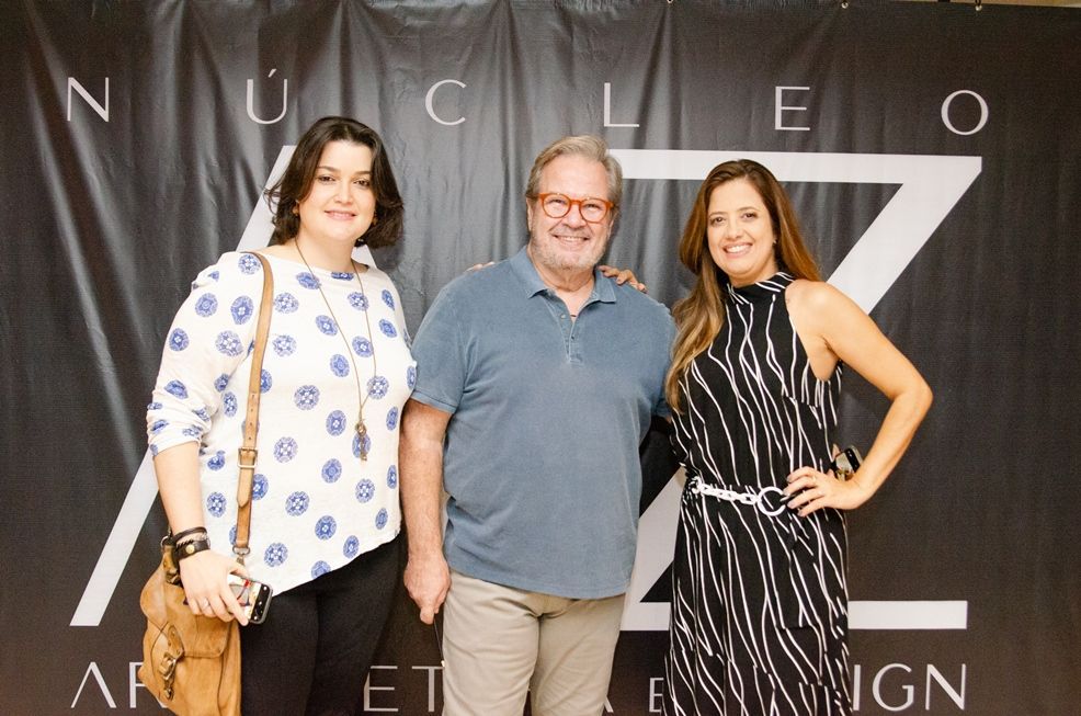 Três pessoas estão posando para uma foto em frente a uma placa que diz nucleo