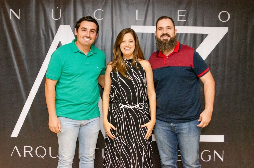 Três pessoas estão posando para uma foto em frente a uma placa que diz nucleo