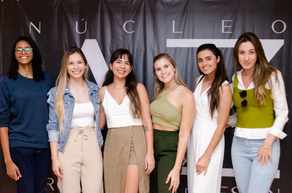 Um grupo de mulheres está posando para uma foto em frente a uma placa que diz nucleo.