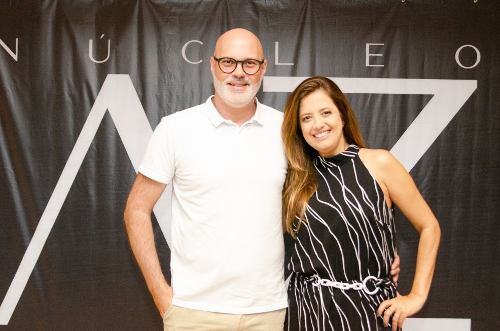 Um homem e uma mulher posam para uma foto em frente a uma placa que diz nucleo