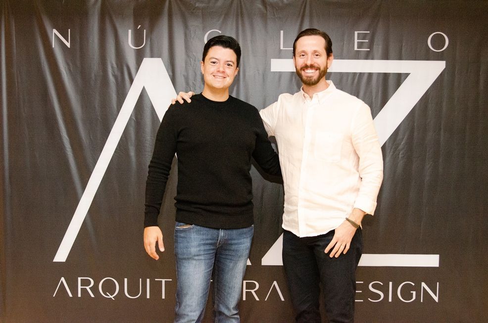 Dois homens posam para uma foto em frente a uma placa que diz arquiteta design