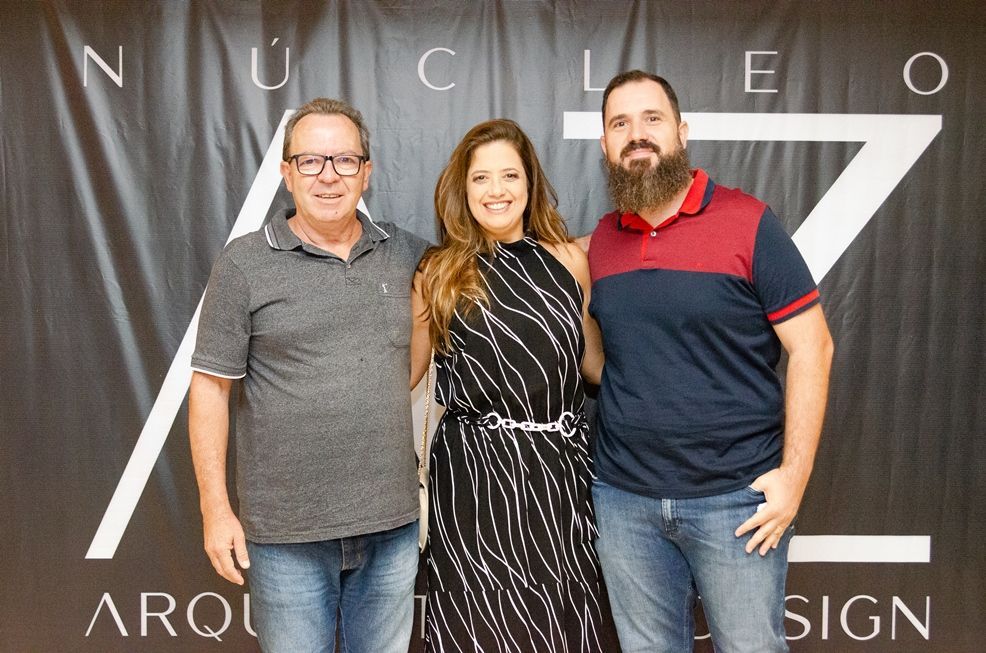 Três pessoas estão posando para uma foto em frente a uma placa que diz nucleo