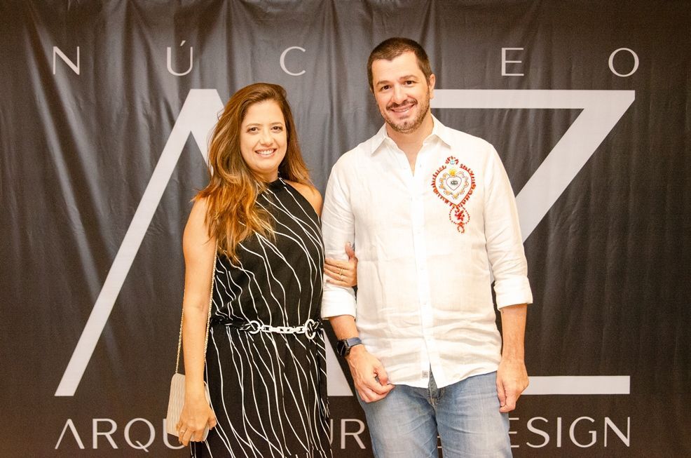 Um homem e uma mulher estão posando para uma foto em frente a uma placa que diz nucleo