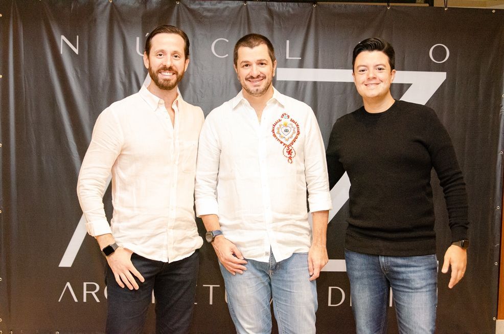 Três homens estão posando para uma foto em frente a uma placa que diz nucleo