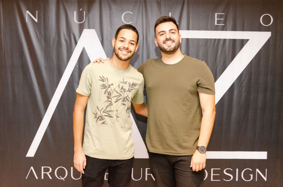 Dois homens posam para uma foto em frente a uma placa que diz arquitetura design