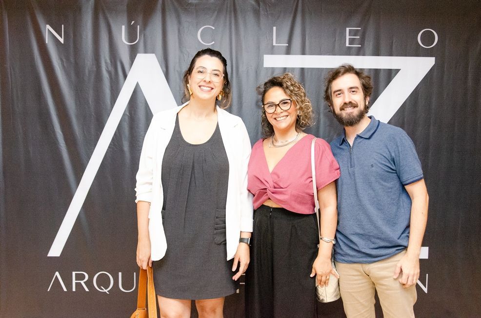 Três pessoas estão posando para uma foto em frente a uma placa que diz núcleo arqui