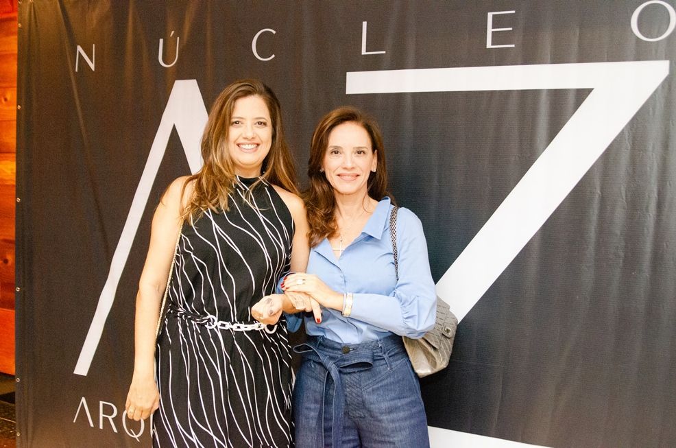 Duas mulheres estão em pé na frente de uma placa que diz nucleo