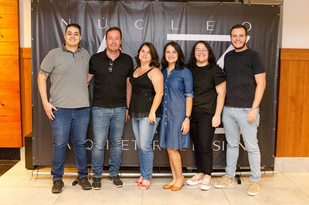 Um grupo de pessoas está posando para uma foto em frente a uma placa.