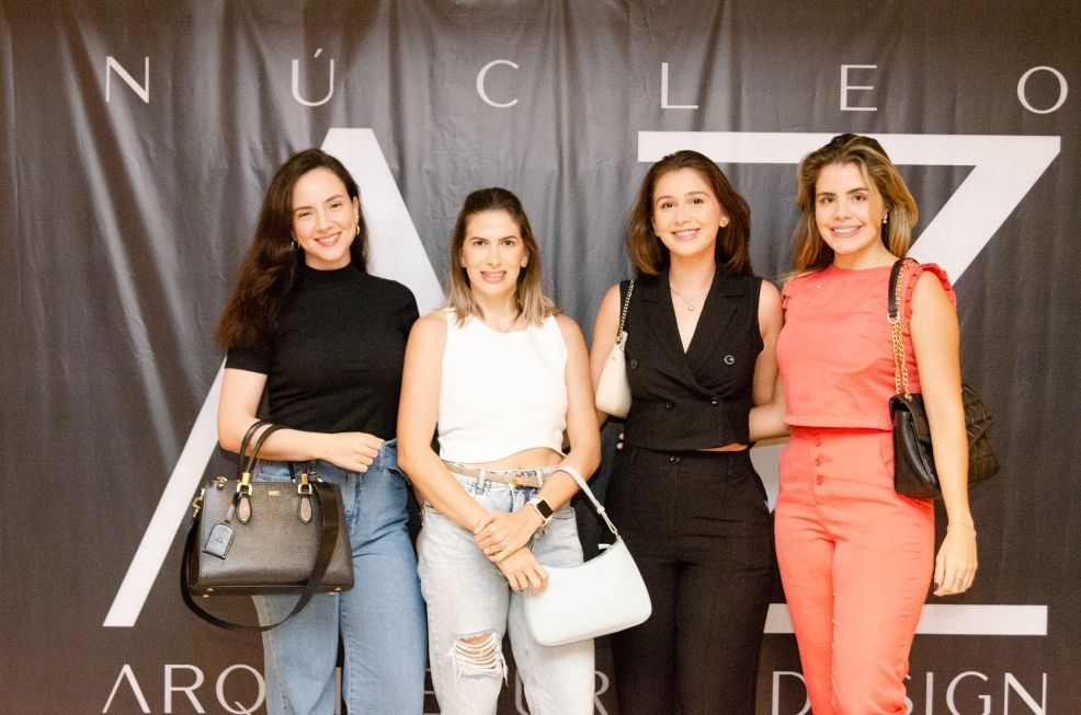 Quatro mulheres estão posando para uma foto em frente a uma placa que diz nucleo