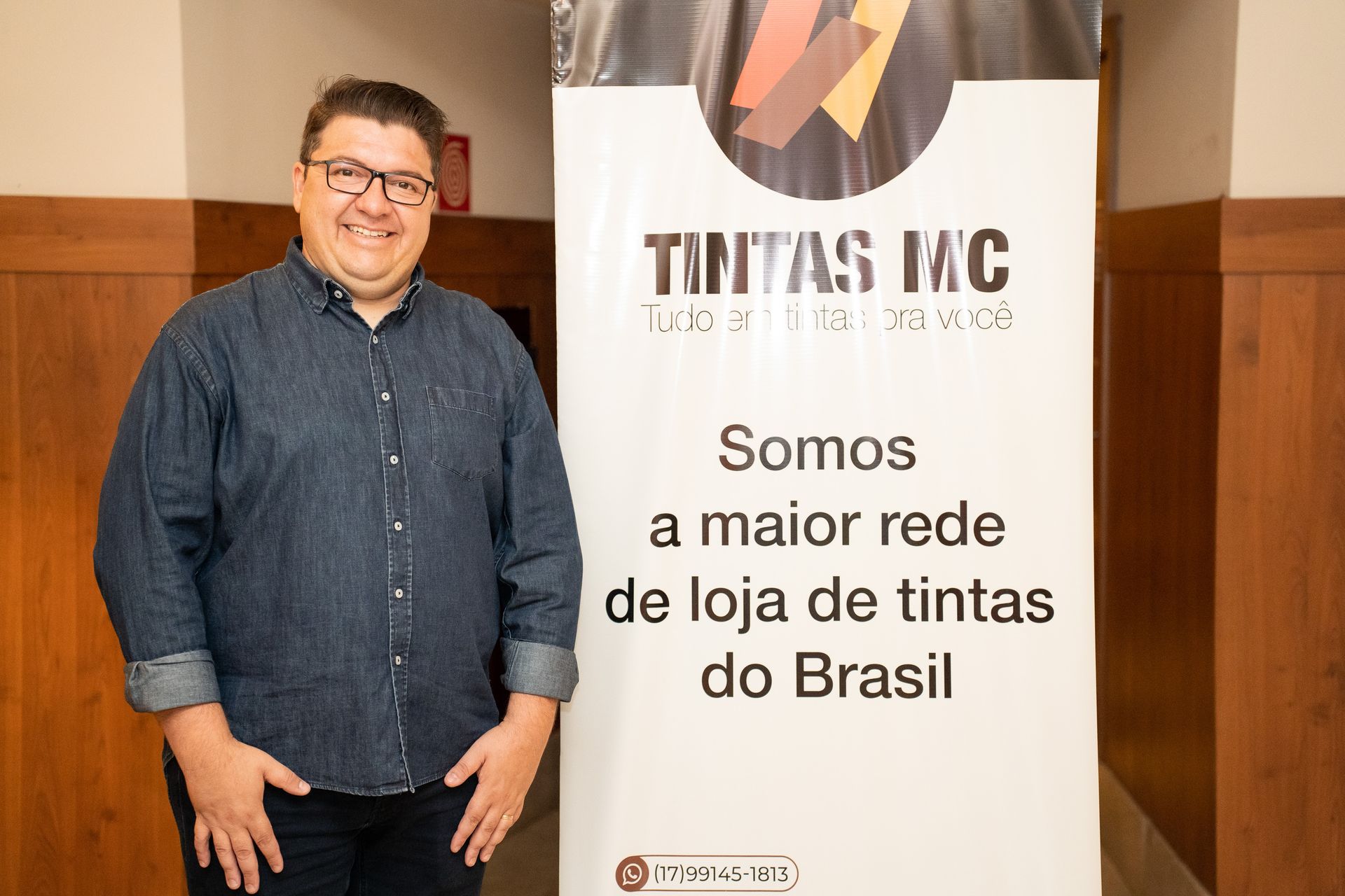 A man is standing in front of a sign that says somos a maior rede de loja de tintas do brasil.