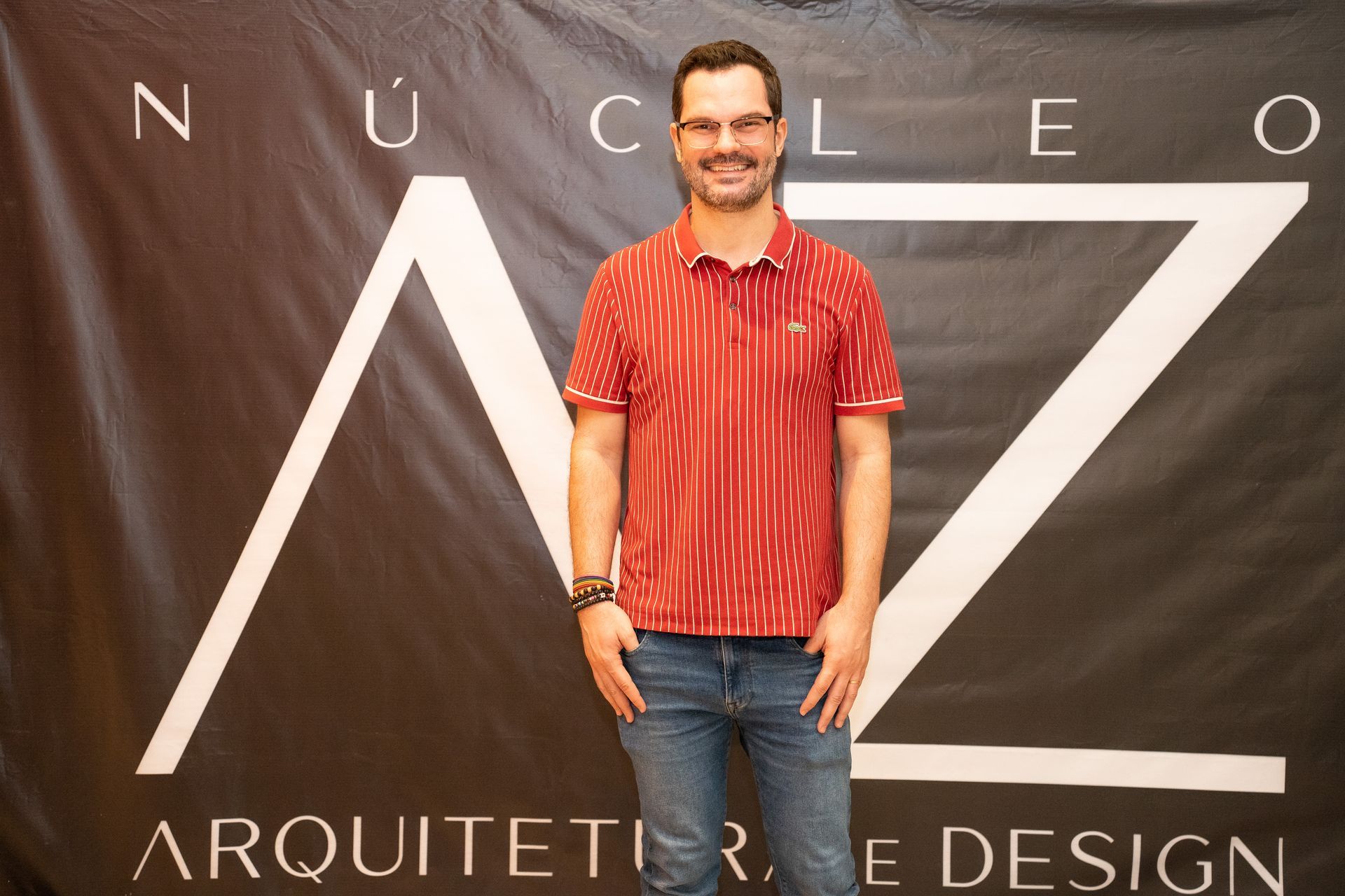 Um homem de camisa vermelha está em frente a uma placa que diz nucleo