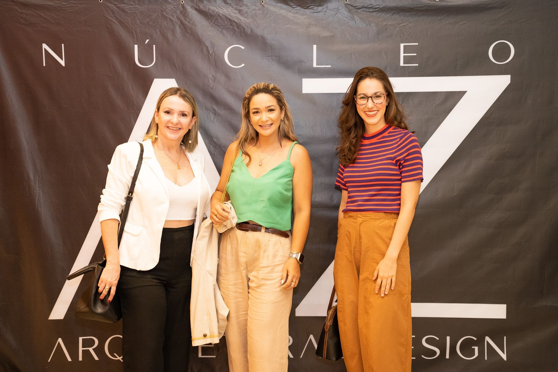 Três mulheres estão posando para uma foto em frente a uma placa que diz nucleo