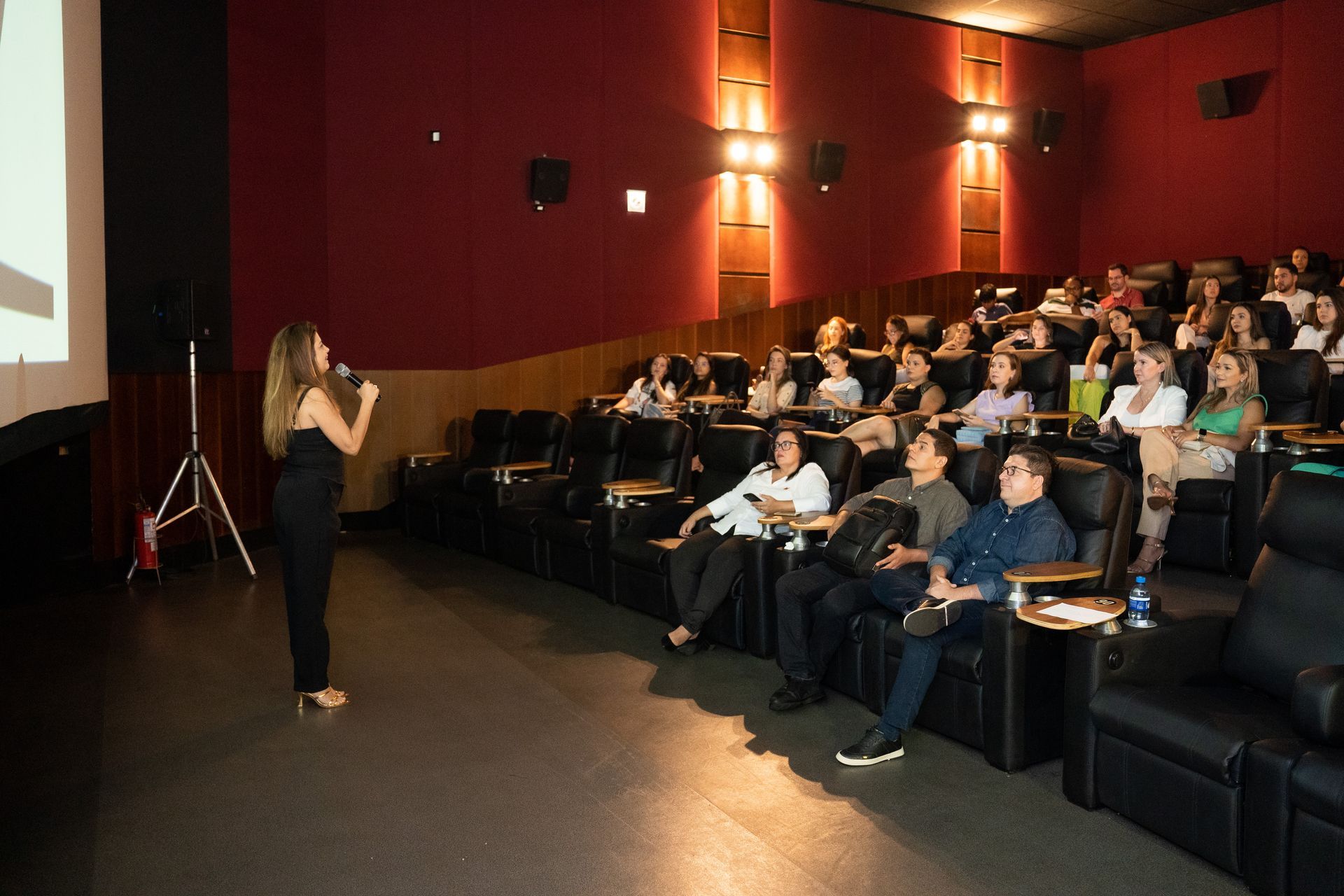 Uma mulher está fazendo uma apresentação para um grupo de pessoas em um cinema.