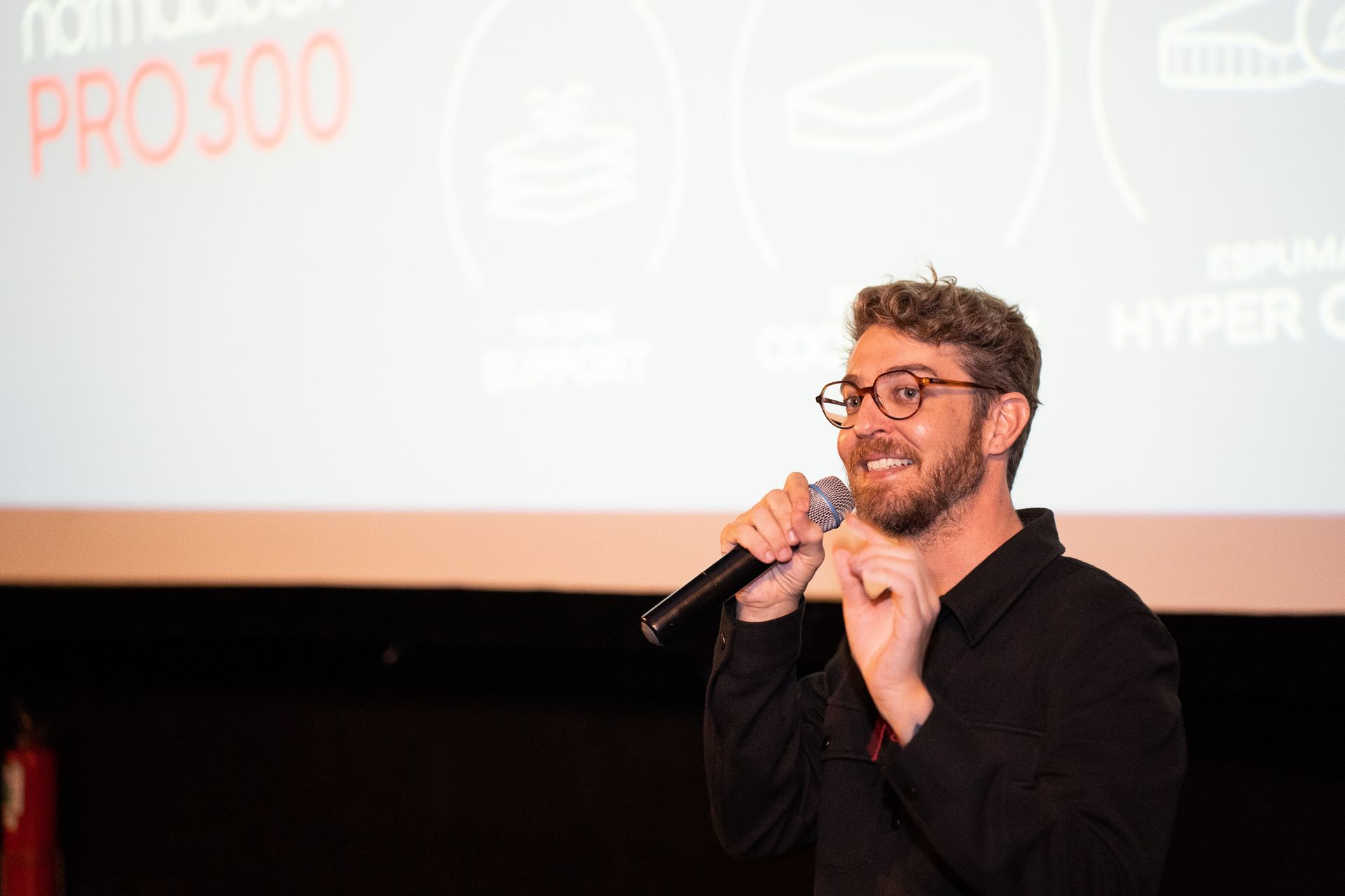 Um homem está segurando um microfone em frente a uma tela grande.