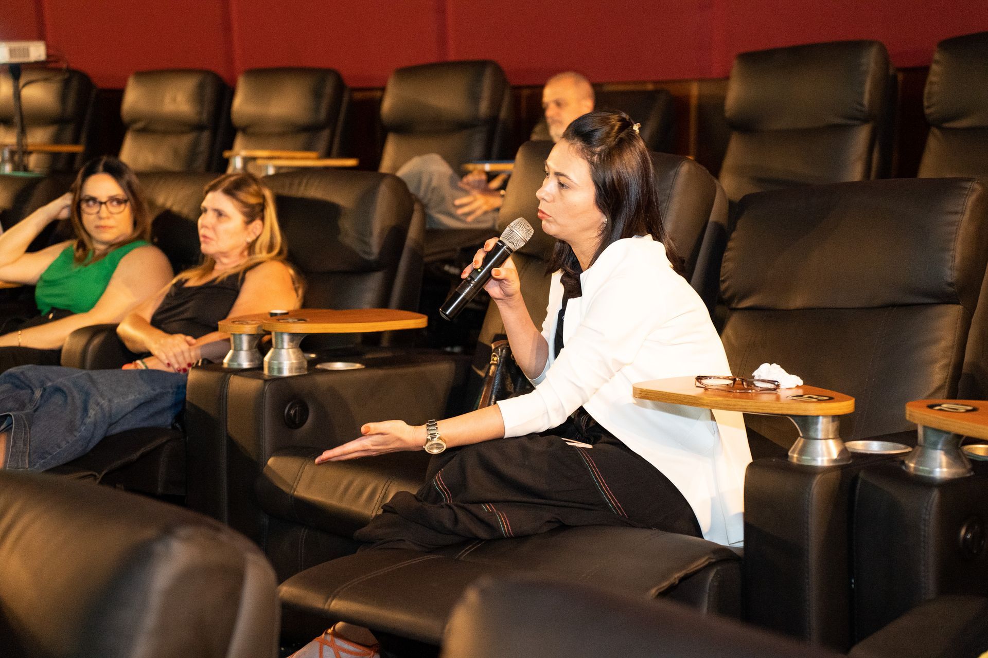 Uma mulher segura um microfone enquanto está sentada em um cinema.