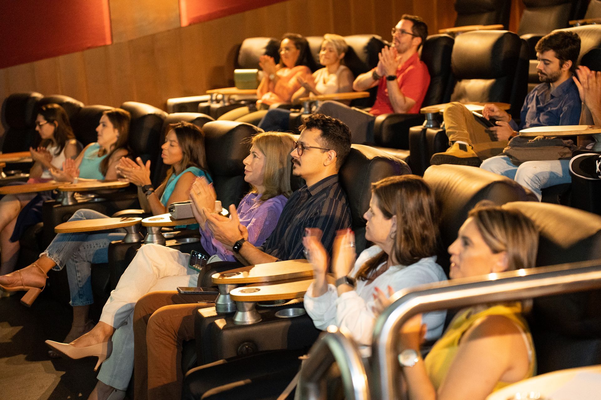 Um grupo de pessoas está sentado em um teatro aplaudindo.