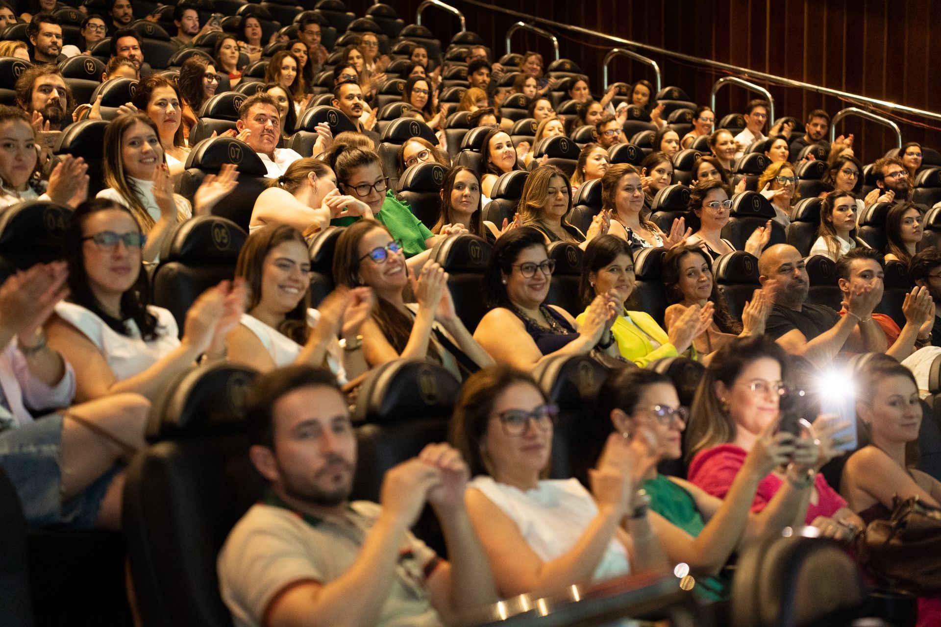 Um grande grupo de pessoas está sentado em um teatro aplaudindo.