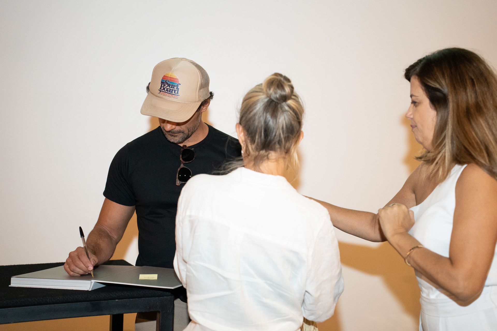 Um homem assina um documento enquanto duas mulheres observam.