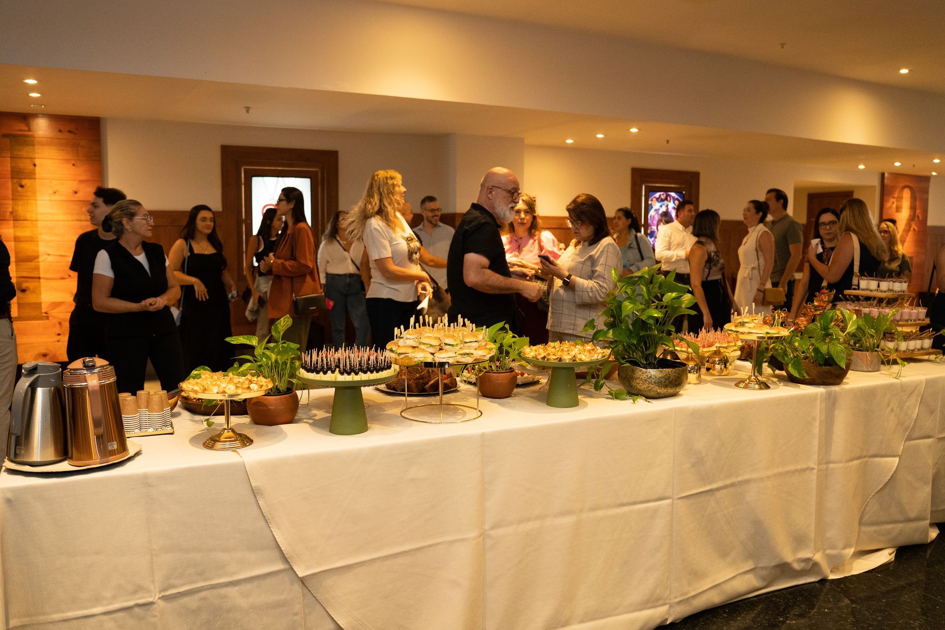 Um grupo de pessoas está de pé ao redor de uma longa mesa com comida.