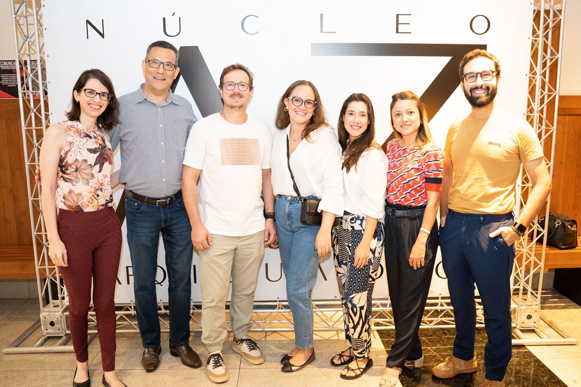 Um grupo de pessoas está posando para uma foto em frente a uma placa que diz nucleo.