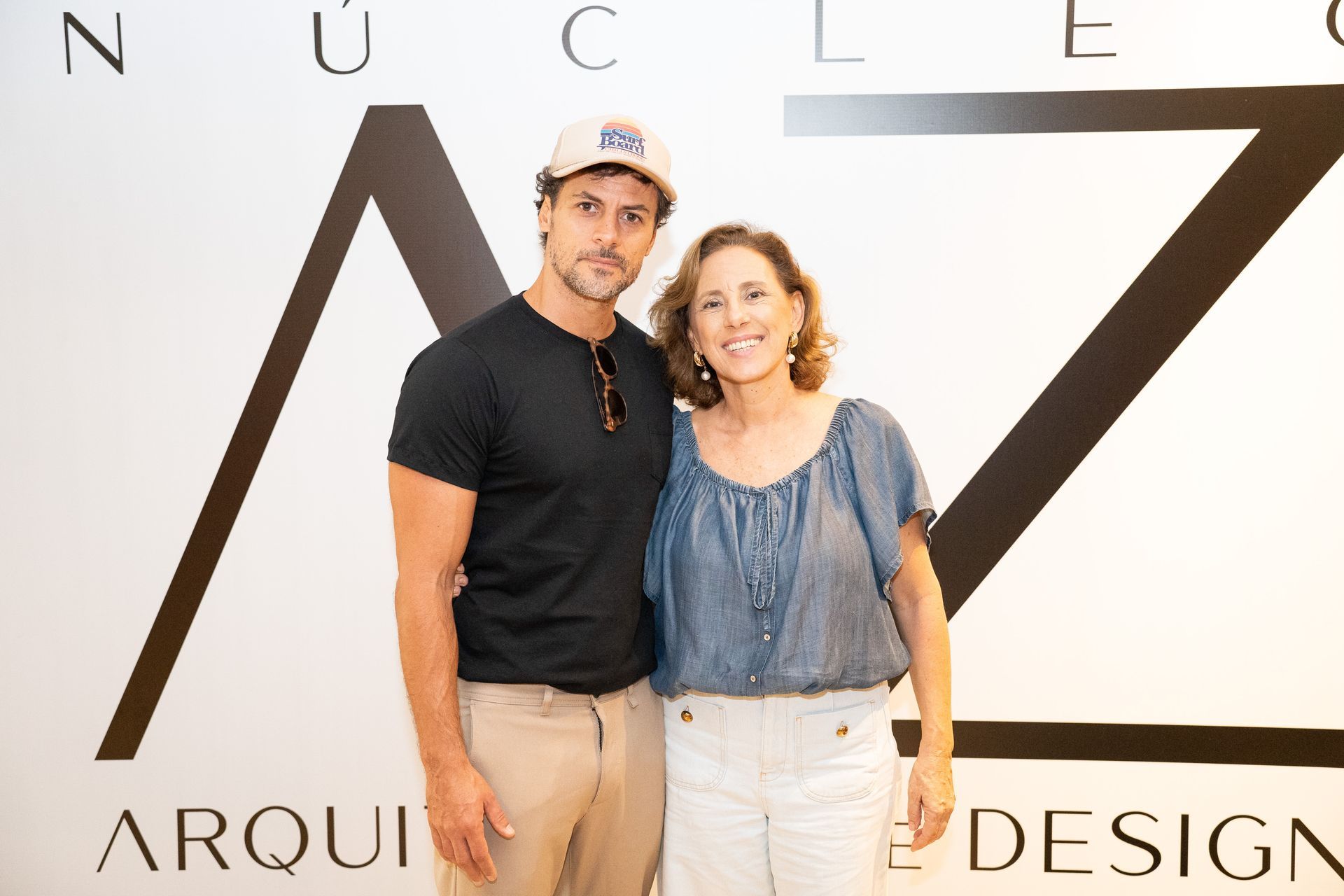 Um homem e uma mulher estão posando para uma foto em frente a uma placa que diz arqui design