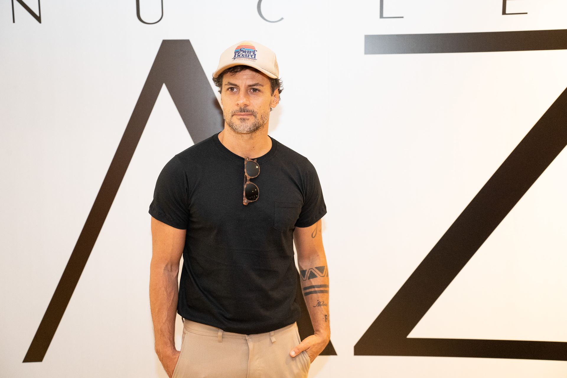 Um homem usando chapéu e óculos de sol está parado em frente a uma grande letra z.