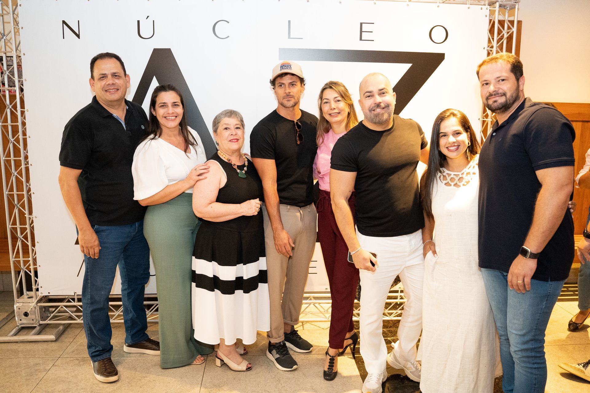 Um grupo de pessoas em pé, uma ao lado da outra, em frente a uma placa que diz nucleo.