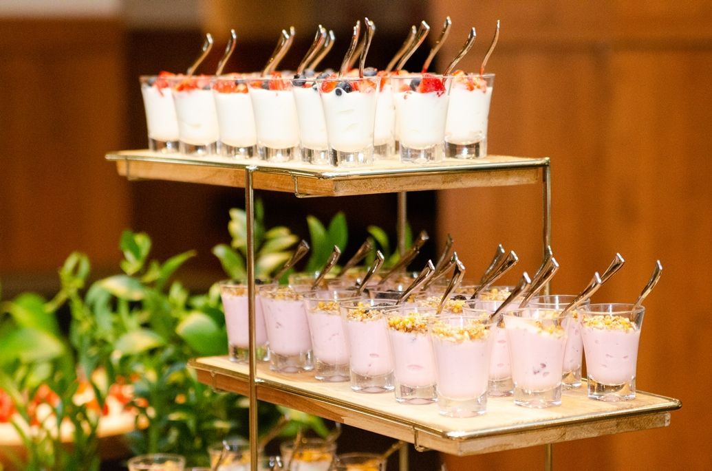 Uma exposição de sobremesas em copos de shot com colheres sobre uma mesa.