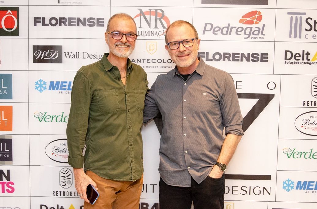 Dois homens estão posando para uma foto em frente a uma parede com logotipos.