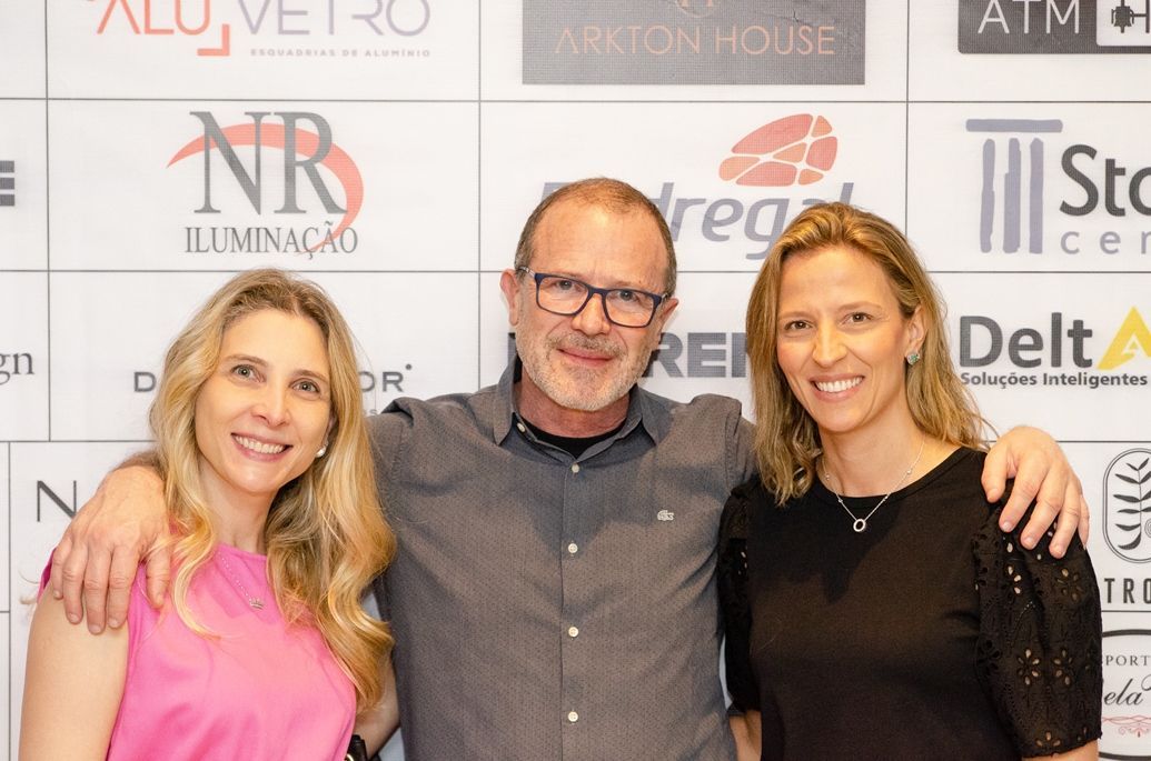 Um homem e duas mulheres estão posando para uma foto em frente a uma parede com logotipos.