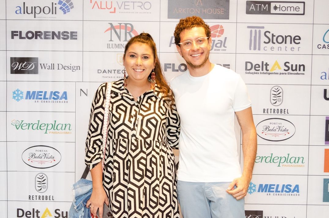 Um homem e uma mulher estão posando para uma foto em frente a uma parede de logotipos.