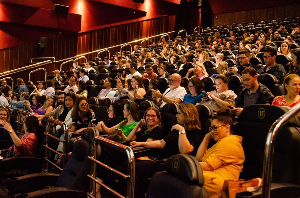 Um grande grupo de pessoas está sentado em um cinema assistindo a um filme.