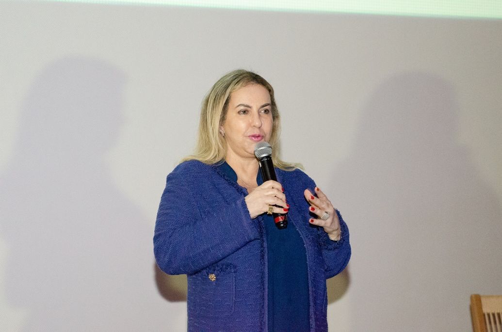 Uma mulher de jaqueta azul está falando em um microfone.