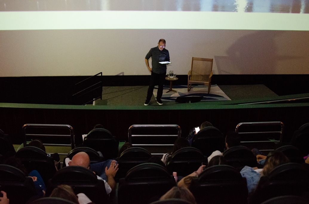 Um homem está em pé em um palco em frente a uma multidão de pessoas.
