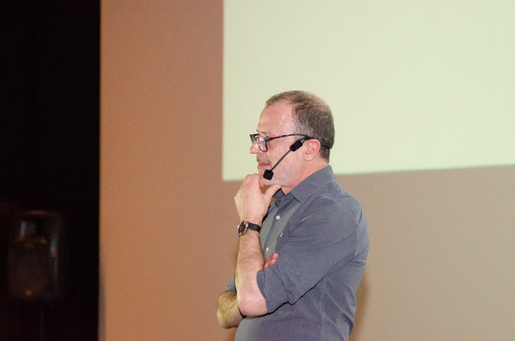 Um homem usando óculos e um microfone está fazendo uma apresentação.