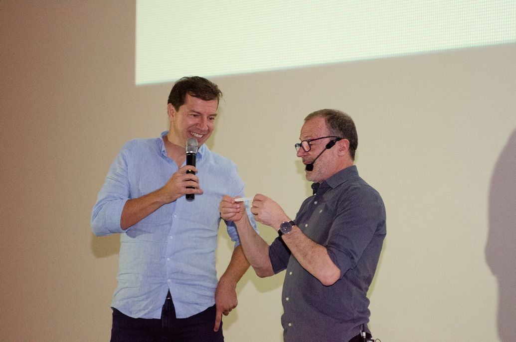 Dois homens estão de pé um ao lado do outro e um deles está segurando um microfone.