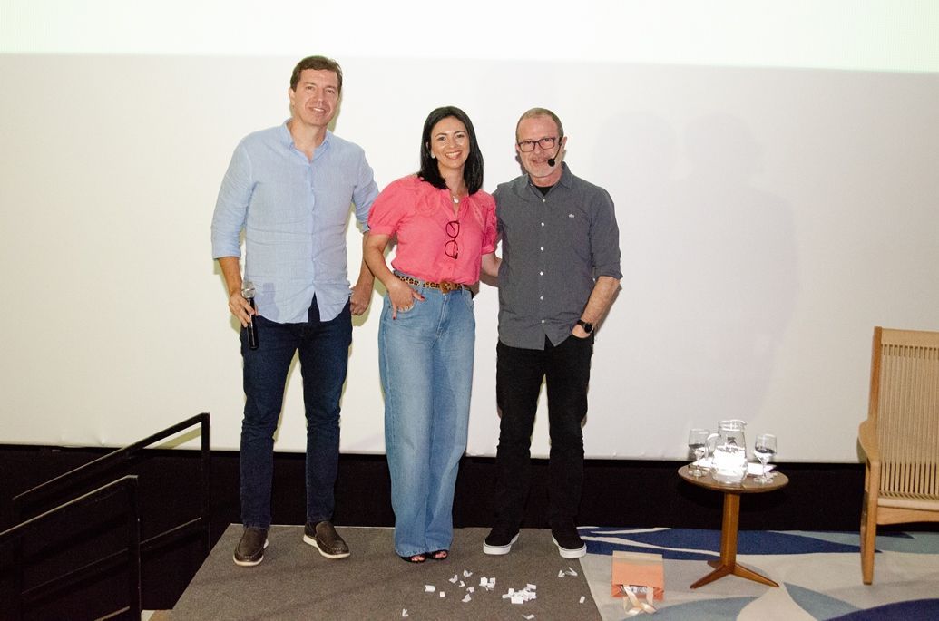Três pessoas estão posando para uma foto em frente a uma tela.
