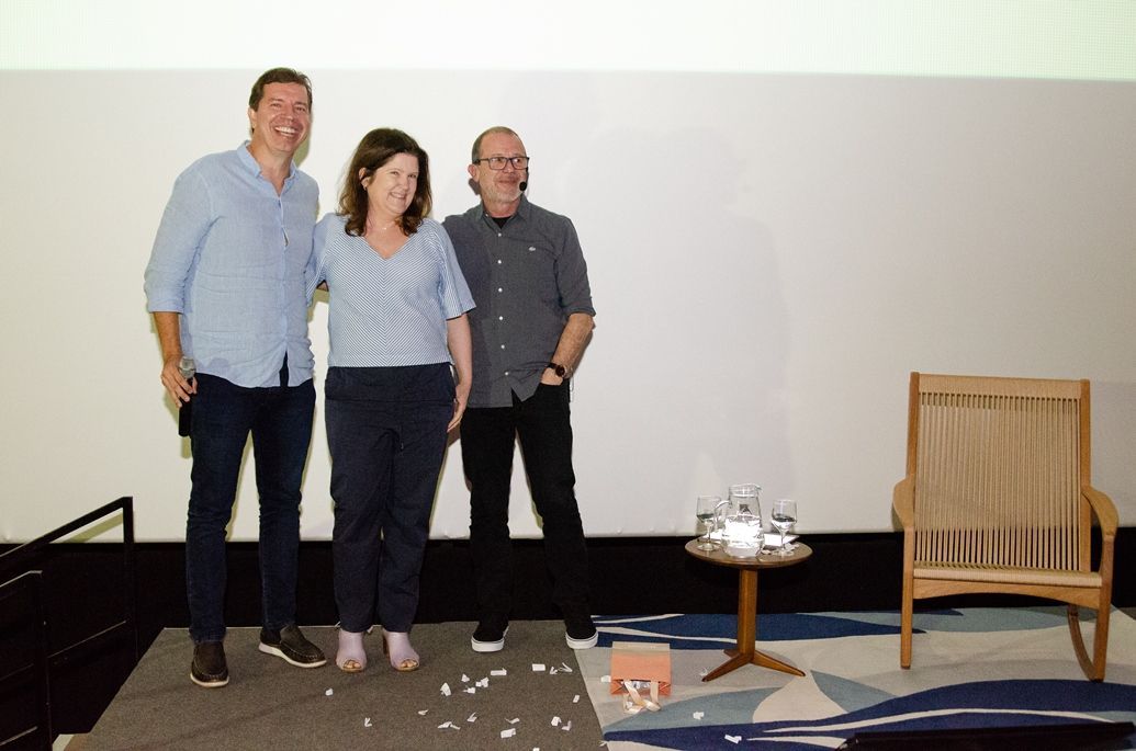 Um grupo de pessoas em pé, uma ao lado da outra, em frente a uma parede branca.