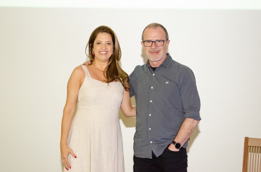Um homem e uma mulher estão posando para uma foto em frente a uma parede branca.