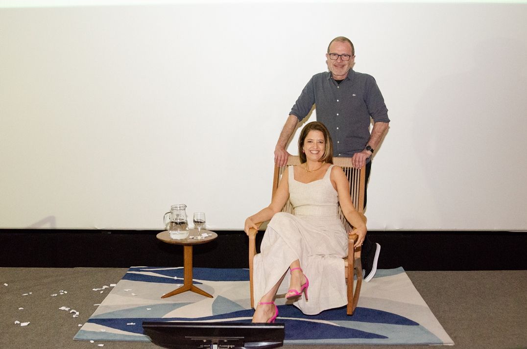 Um homem está de pé ao lado de uma mulher sentada em uma cadeira.