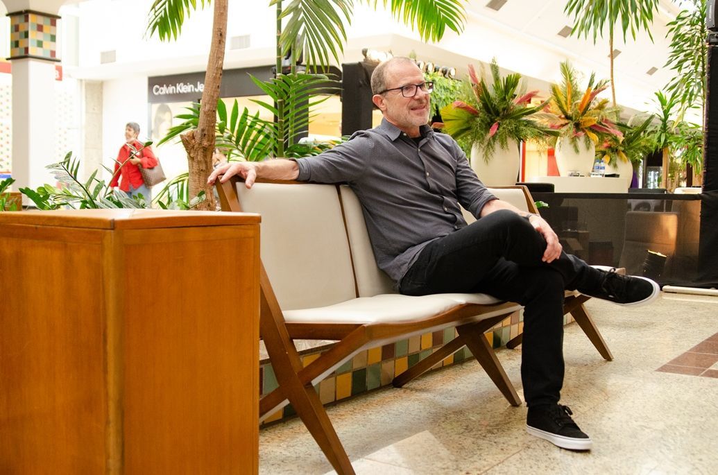 Um homem está sentado em um banco de madeira em um shopping.