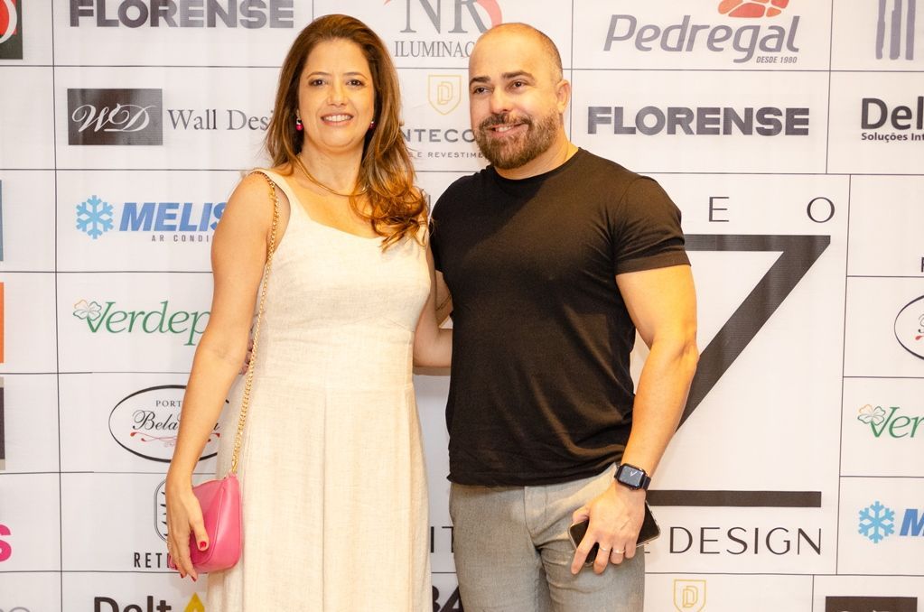 Um homem e uma mulher estão posando para uma foto em frente a uma parede com logotipos.