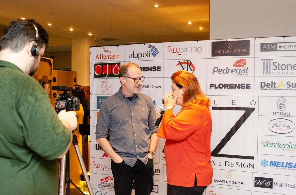 Um homem está tirando uma foto de uma mulher conversando com um homem em frente a uma parede com logotipos.