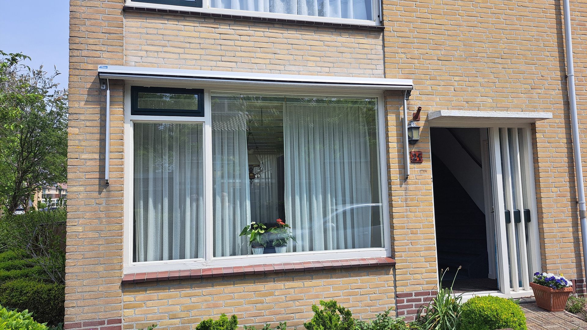 Een bakstenen huis met een groot raam en witte gordijnen.
