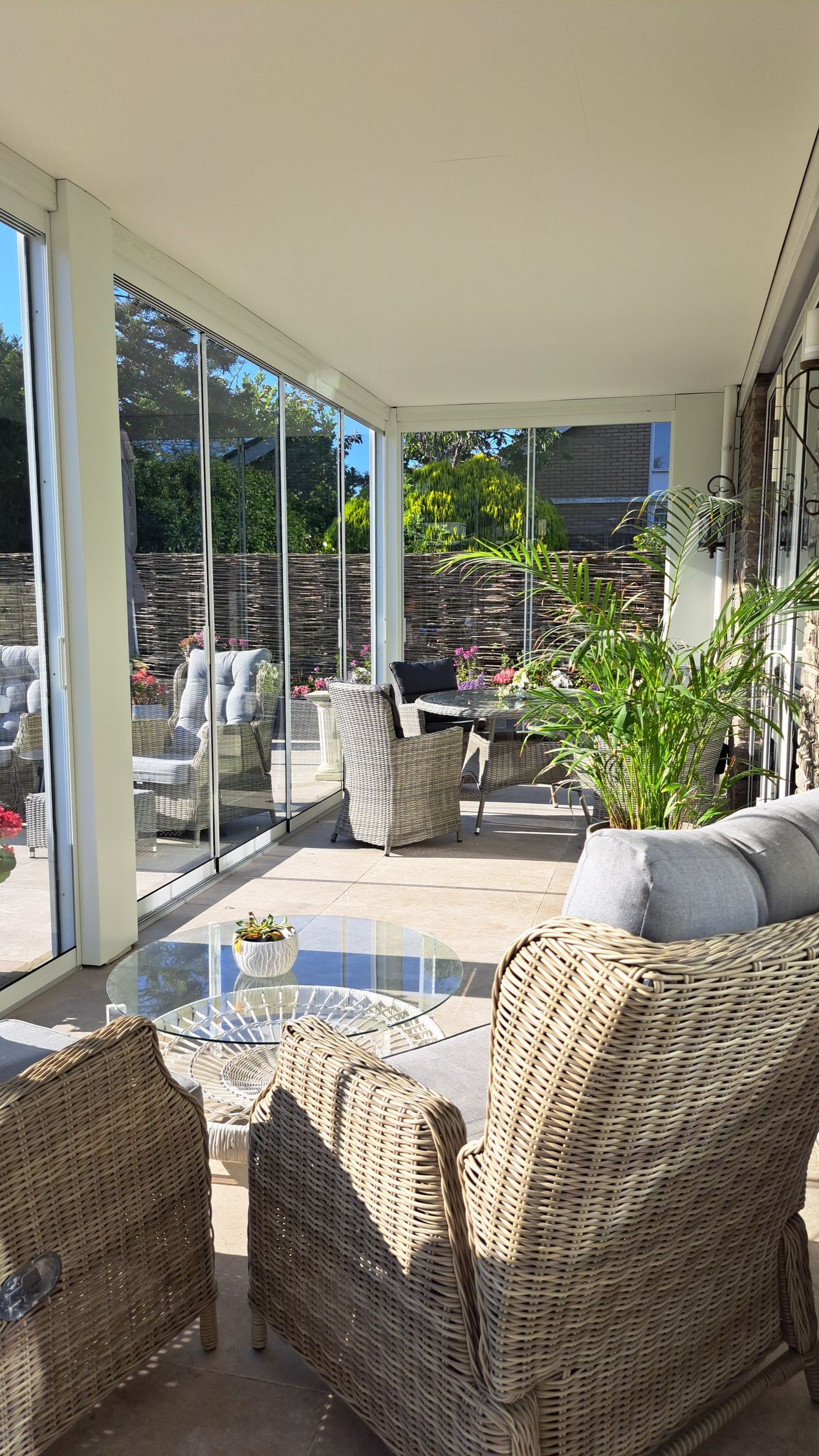 Een terras met rieten meubels en een glazen tafel.