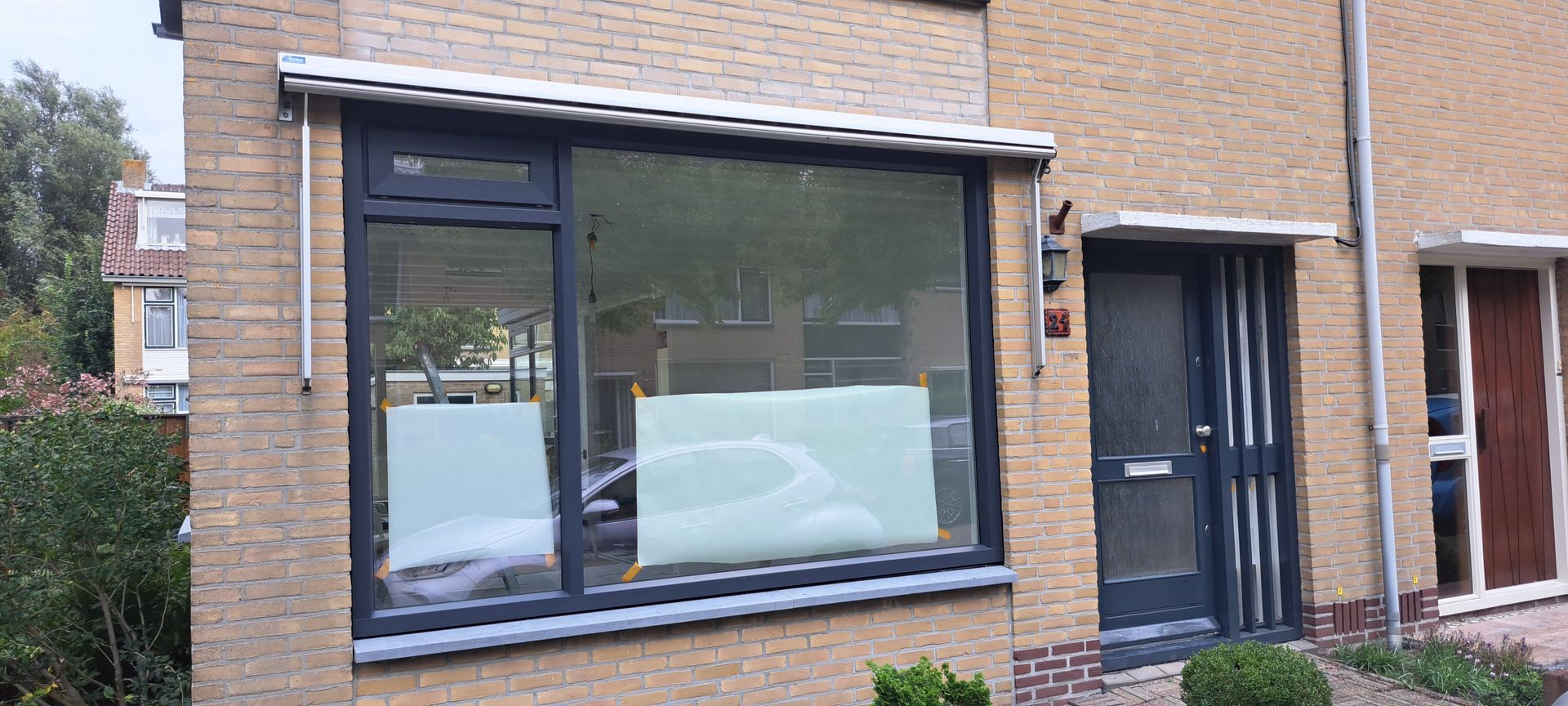 Een bakstenen huis met een groot raam en een zwarte deur.